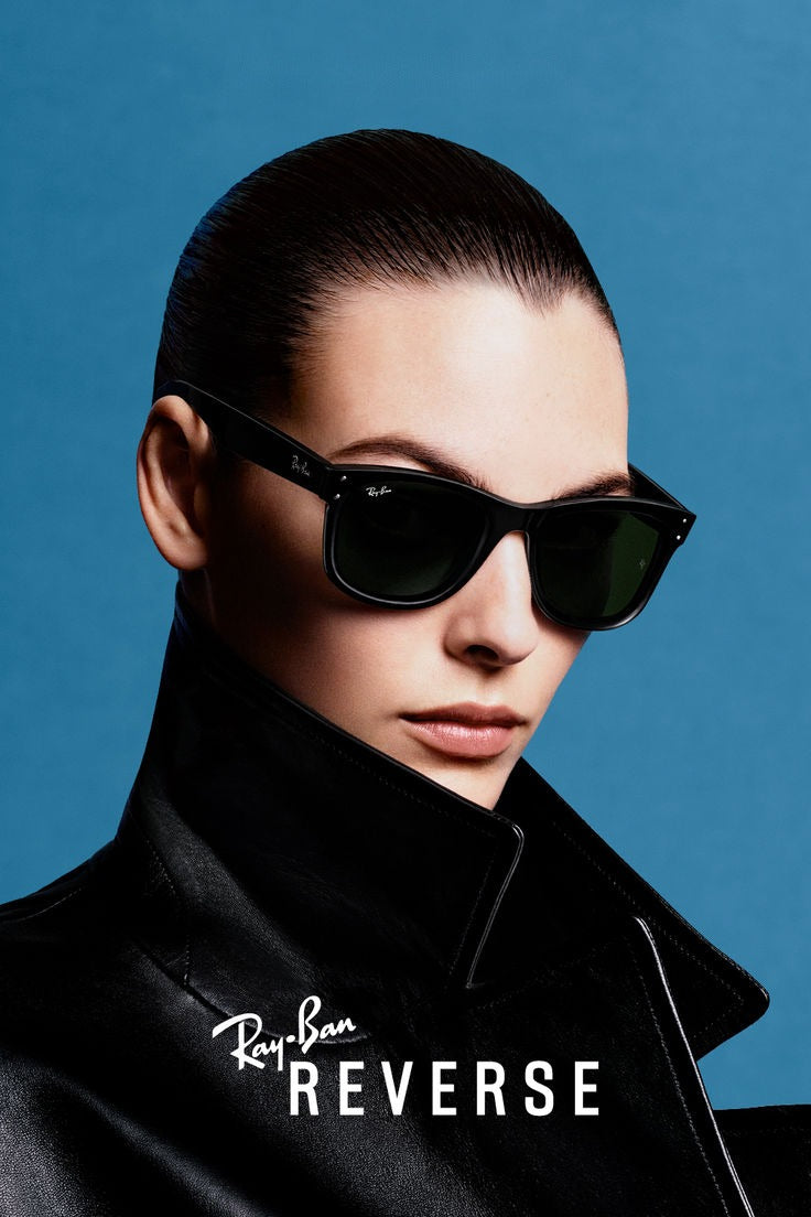 Model wearing black sunglasses against a blue backdrop